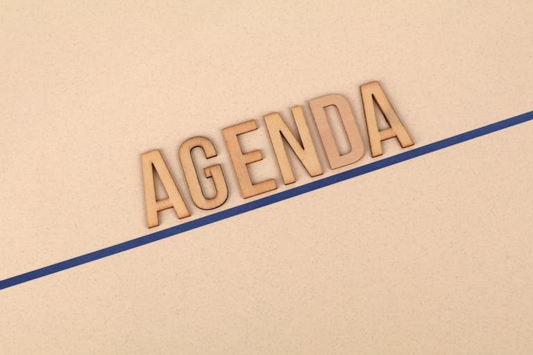 Close-up of wooden 'AGENDA' letters on a beige surface with a blue line, studio setting.