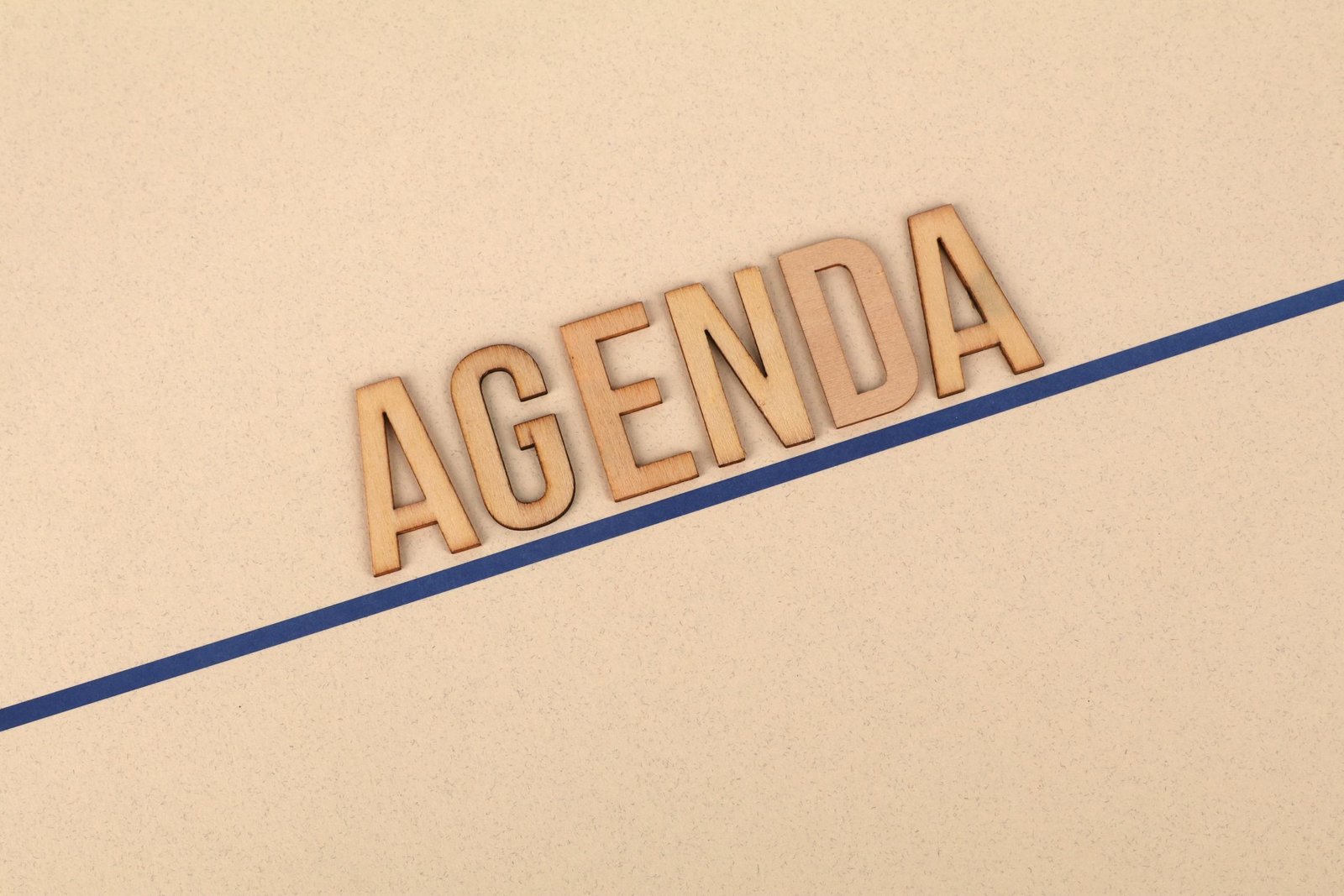 Close-up of wooden 'AGENDA' letters on a beige surface with a blue line, studio setting.